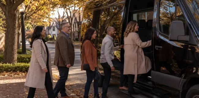 A suburban group boarding a black executive van on an autumn afternoon