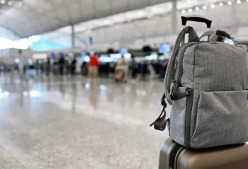 A gray backpack on top of a rolling suitcase in an airport terminal