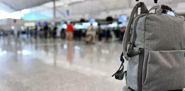 A gray backpack on top of a rolling suitcase in an airport terminal