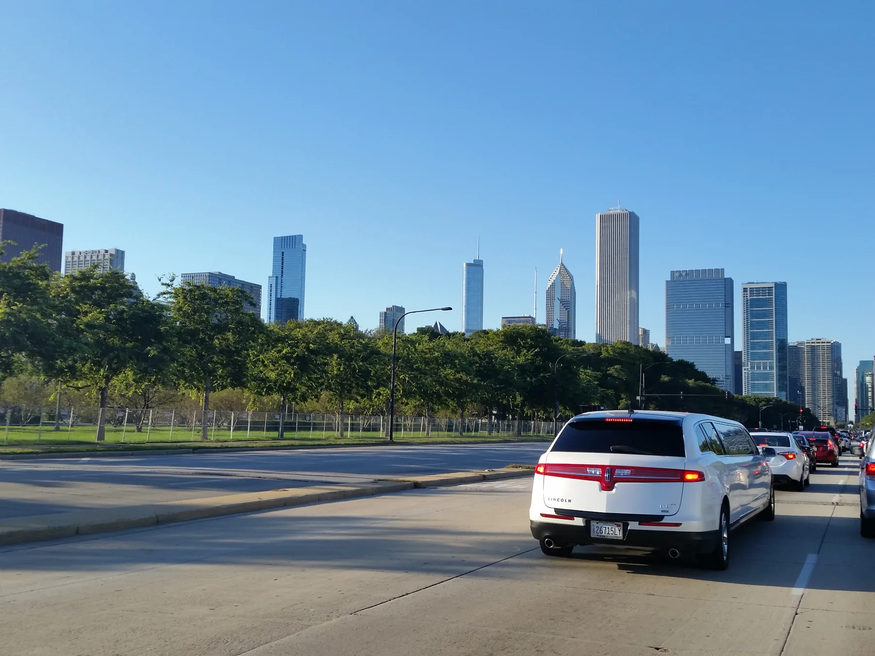 A white limousine in street traffic with the Chicago skyline beyond trees