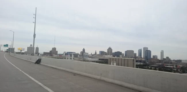 Milwaukee skyline beyond a highway barrier under an overcast sky